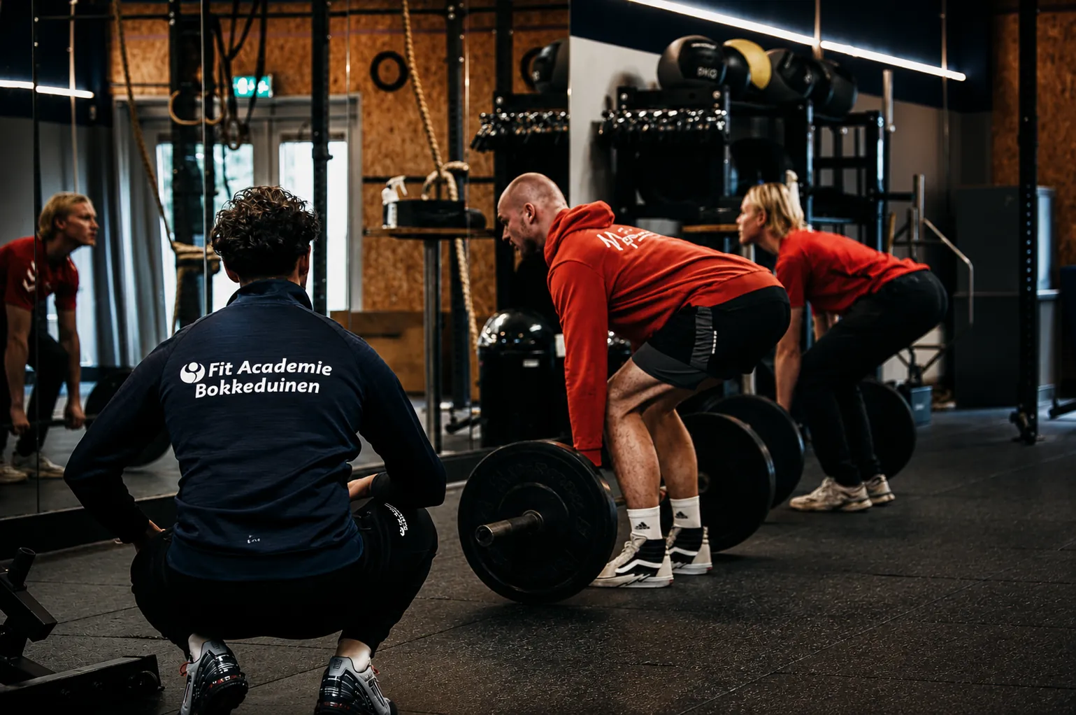 Drie atleten trainen met barbells onder begeleiding